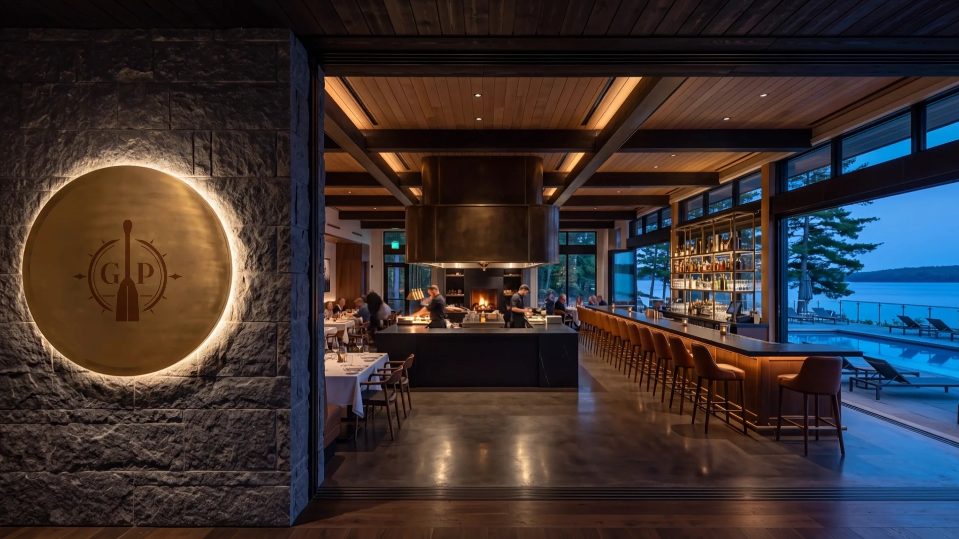 Warm backlit Gilded Paddle emblem beside the centre open kitchen, long lounge bar, outdoor pool and Lake Muskoka at blue hour